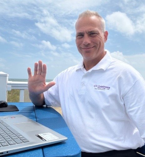 CodeBreeze Solutions founder Kevin Mohan at the beach with laptop, waving